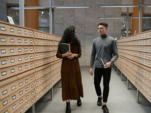 A student and professor in conversation as they walk in a library.