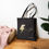 Thumbnail: Black cotton canvas tote bag with big lightning Pin image stands on the floor.