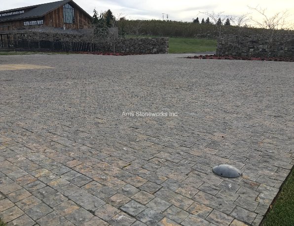 Split cobblestone parking lot paving using rich, earthy Montipora Limestone laid out in a custom radial geometric design.