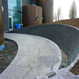 Modern architectural facade featuring a massive curved wall and matching pathway in Black Fossil Marble, highlighting the seamless transition of fossilized textures across vertical and horizontal surfaces.