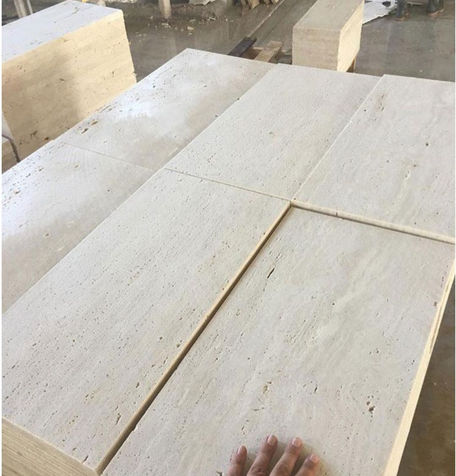 Large beige travertine slabs organized on a factory floor for architectural fabrication.