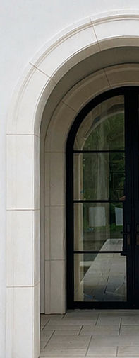 Natural stone cladding detail. A black arched window set deep into a massive natural limestone block facade, highlighting stone depth and architectural profile.