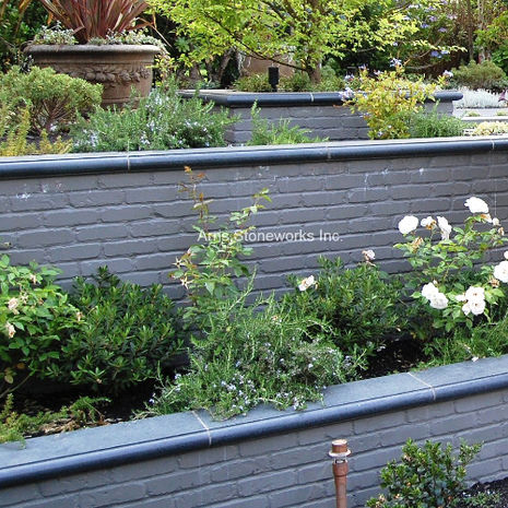 View of the Medina Residence backyard showing layered stone retaining walls and matching Obsidian Basalt pavers.