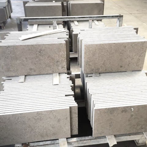 Bundles of thick rectangular grey-beige Light Taupe Limestone cladding stones stacked together in a stone fabrication workshop.