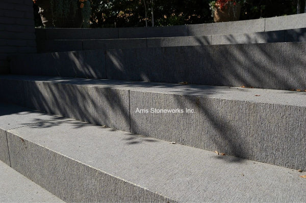 Modern residential landscape with Obsidian Basalt pavers, large section stone stairs, and a sleek water feature with custom stone wall caps.