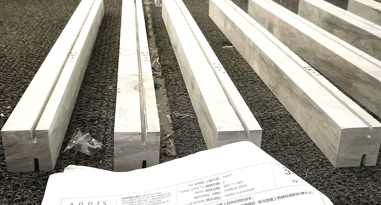 Detailed architectural blueprint drawings and stone fabrication templates placed over cut limestone blocks.