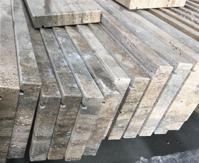 A heavy stack of square grey-toned Titanium Travertine flooring tiles in a stone fabrication facility.