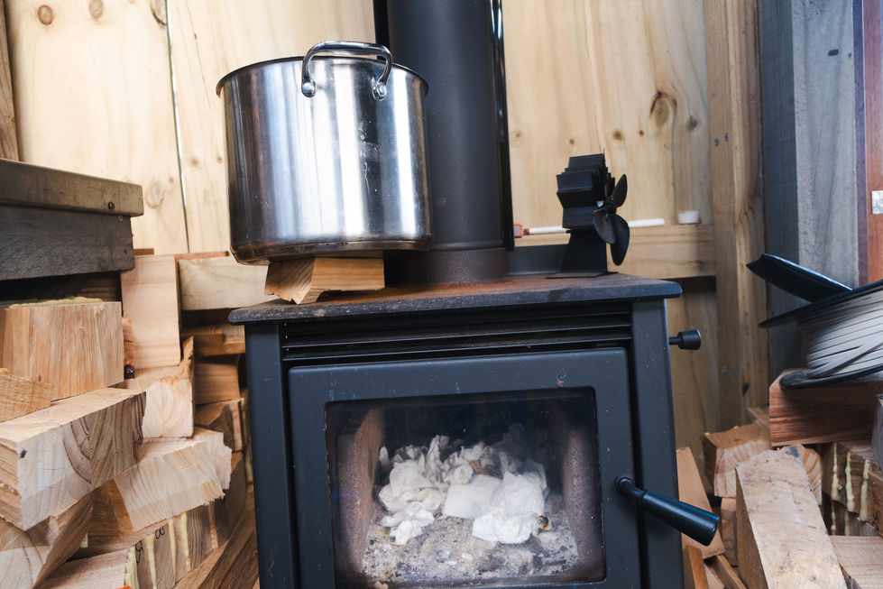 Wood stove with pot, surrounded by stacked firewood.