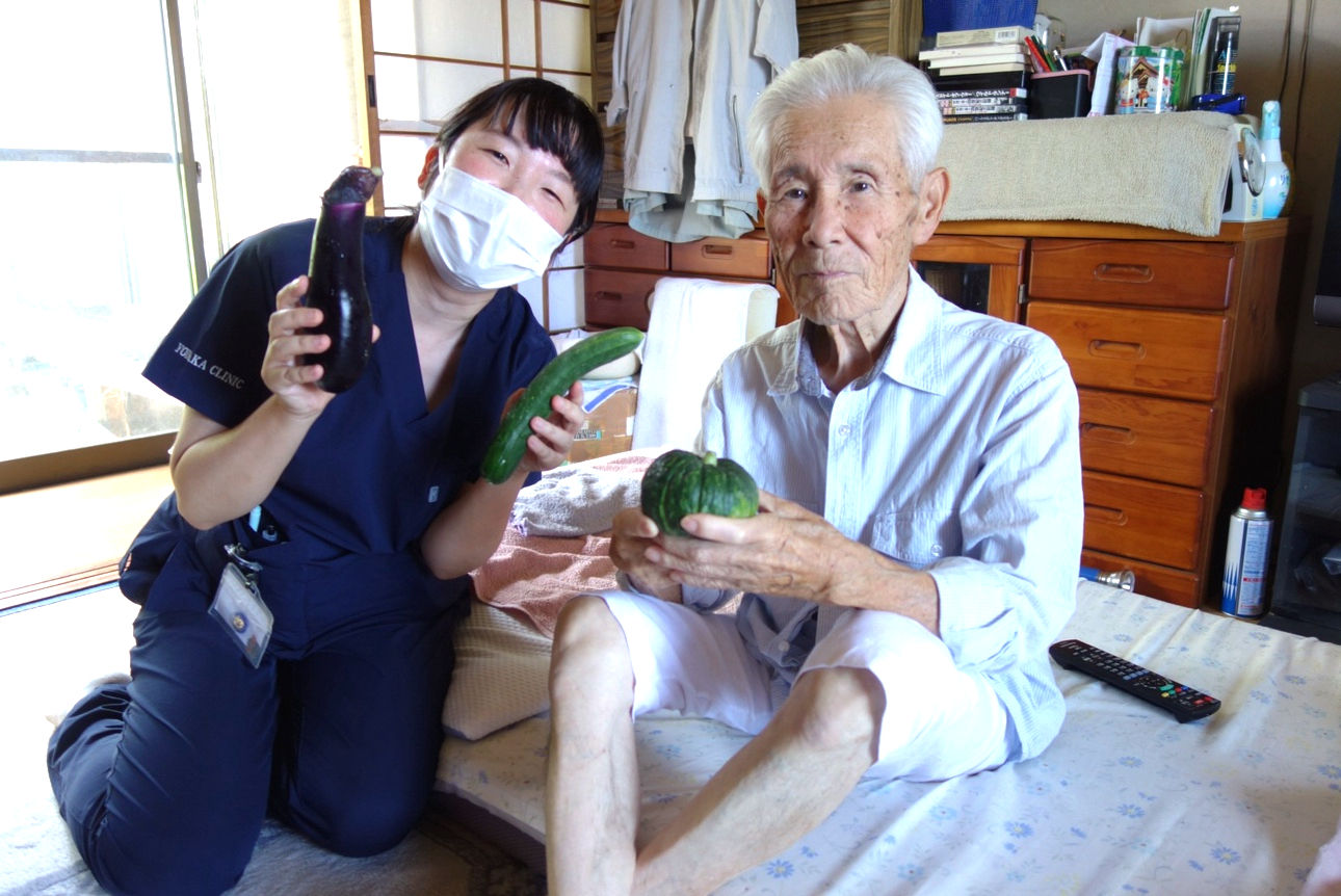 自宅で療養中の高齢男性と医療者が、野菜を手にして一緒に写っている様子