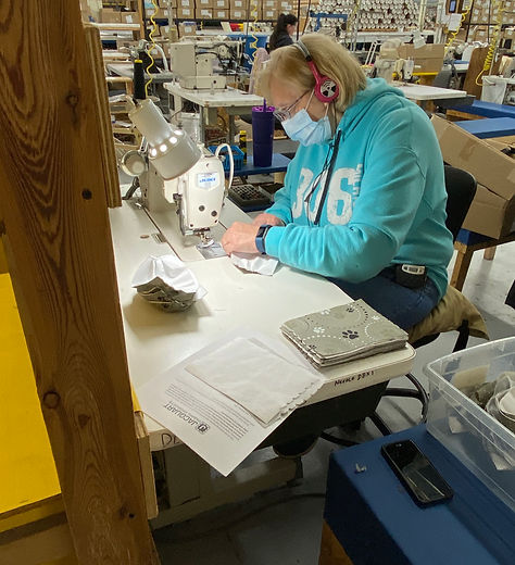 Image of a woman at in a factory at an industrial sewing machine sewing face masks.