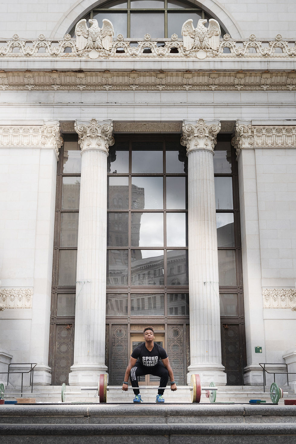 Man preparing to lift a barbell in front of a grand building.