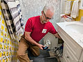 A technician inspecting bathroom plumbing under a sink.