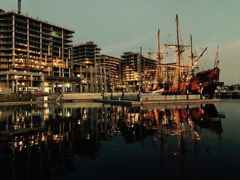 Harbor at night with a tall ship and buildings reflecting in water