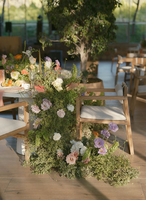Sweetheart table with floral installations cascading over modern wooden chairs, surrounded by soft natural light.