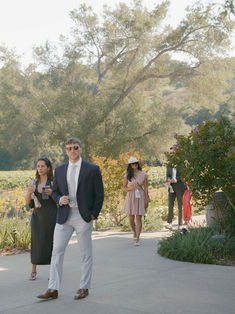 Wedding guest couple posing along a vineyard pathway with olive trees and hillside views at Monserate Winery.