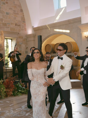 Bride in an off-the-shoulder lace gown entering the reception hand-in-hand with groom, greeted by cheering guests at Monserate Winery.
