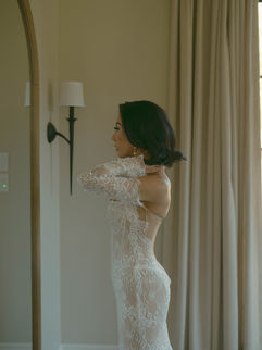 Bride in fitted lace gown adjusting earrings while standing in a softly lit corner of Monserate Winery’s bridal suite.