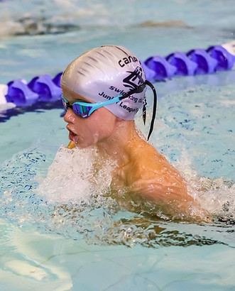 A child in a silver Camp Hill Swimming Club swim cap and blue goggles is swimming in a race