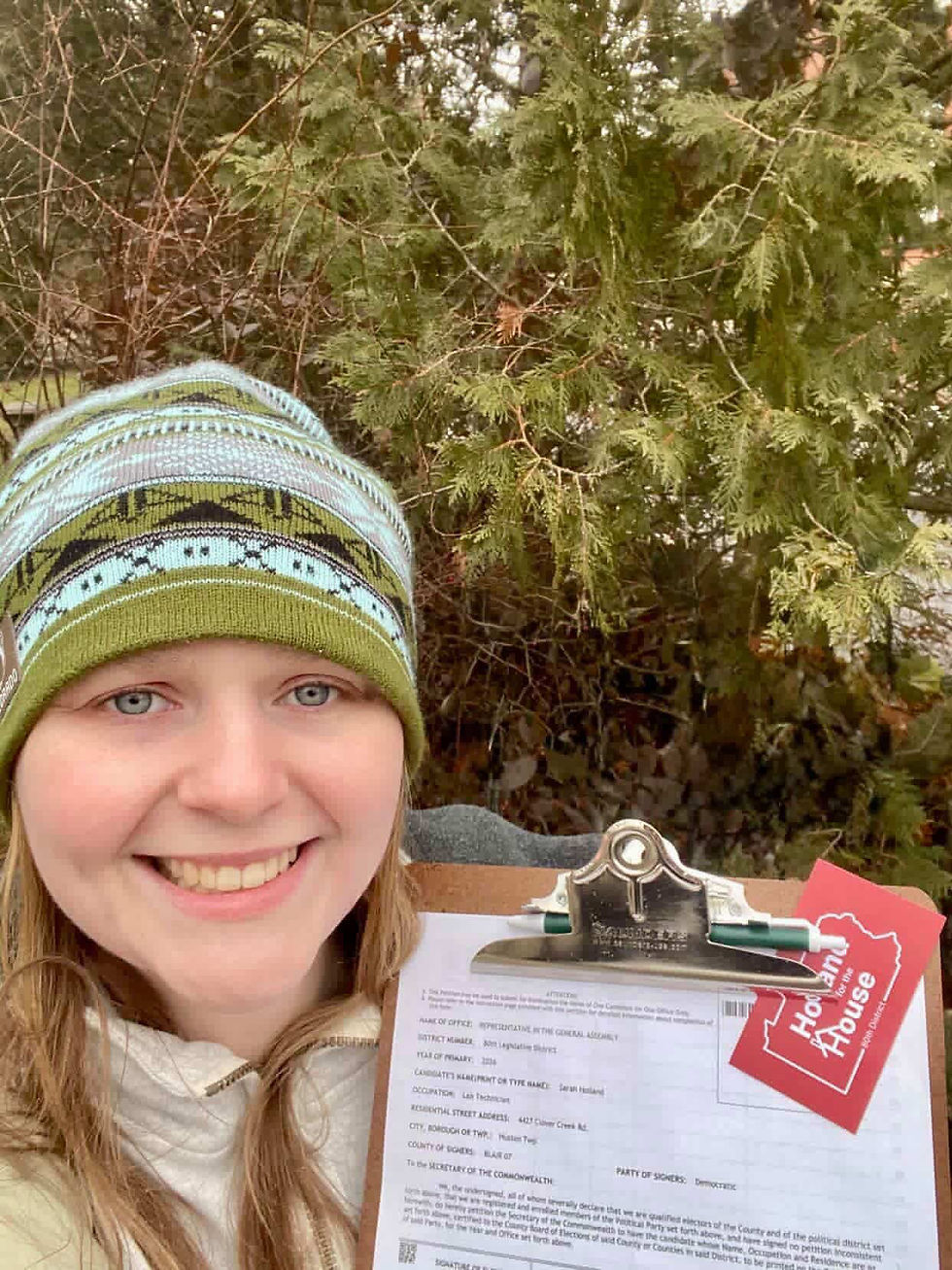 a selfie of Sarah Holland holding up her petition clipboard with her Holland for the House business card on it