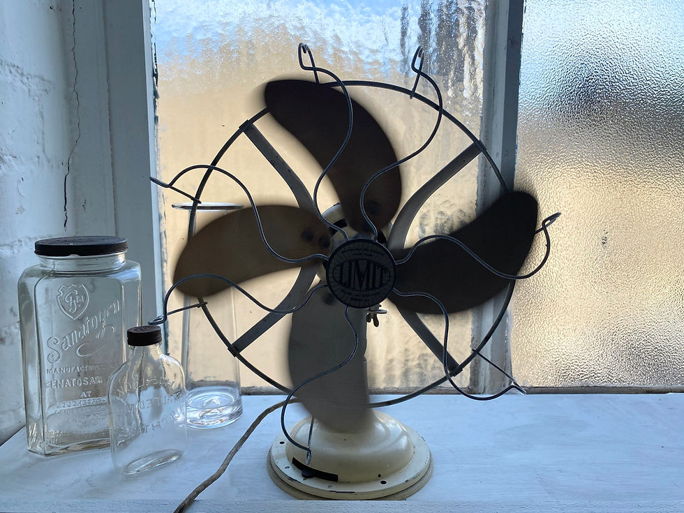 A vintage electric fan silhouetted on a sunny windowsill.