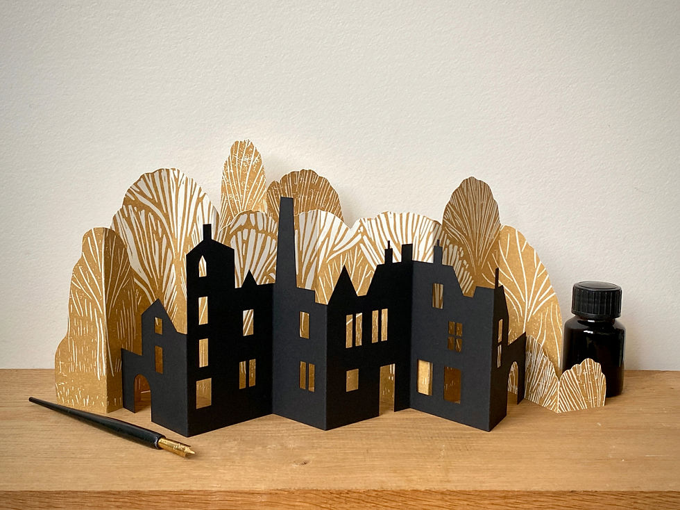 A black paper townscape with golden trees behind on a pale wood shelf.