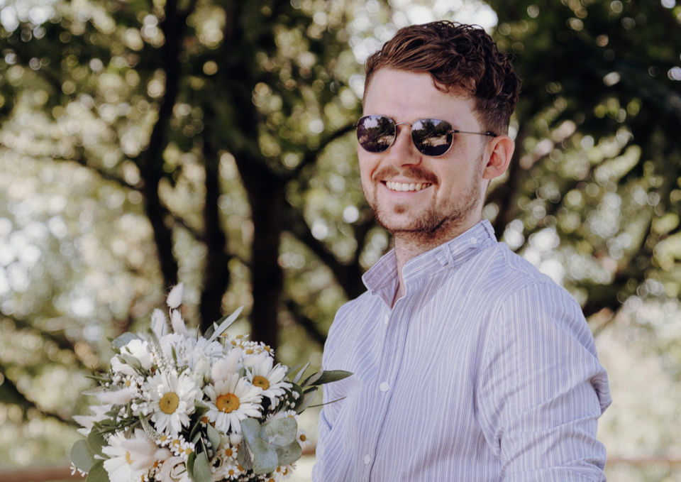 Mann in Tracht mit Sonnenbrille und Brautstrauß im Park