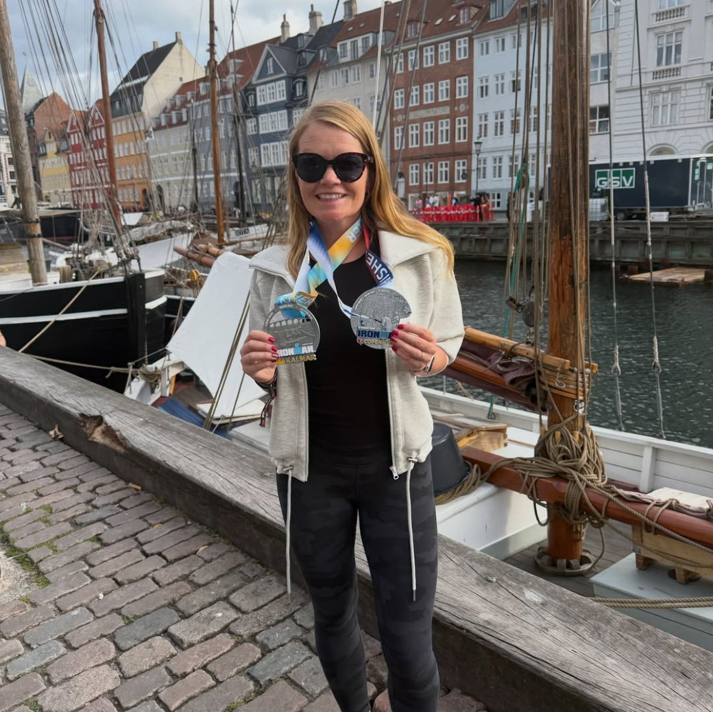 Smiling athlete in sunglasses holds two medals in Nyhavn, Copenhagen.