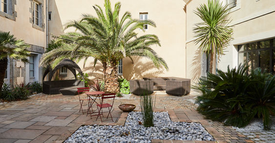 Cour intérieure avec palmiers et salon extérieur, Hôtel Le Petit Périer à Laval
