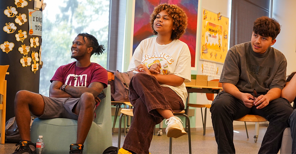 Three people sit indoors, smiling and engaged. Background has bee decorations with "I DREAM TO BE" text. Warm and lively atmosphere.