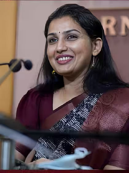 Dr. Renu Raj, IAS, smiles while speaking at a public event, dressed in a maroon saree.