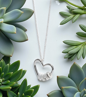 Halskette zwischen grünen Pflanzen der Anhänger ist ein Herz mit 4 weissen runden Steinen | Muttermilchschmuck Schweiz