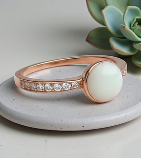 Fingerring liegt auf einem Stein er ist Rosé und hat einen weissen Stein aus Muttermilch am Rand hat er Zirkonias | Muttermilch Schmuck Schweiz