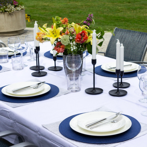 Outdoor table setting featuring blue chargers, tall candles, and a colorful floral arrangement
