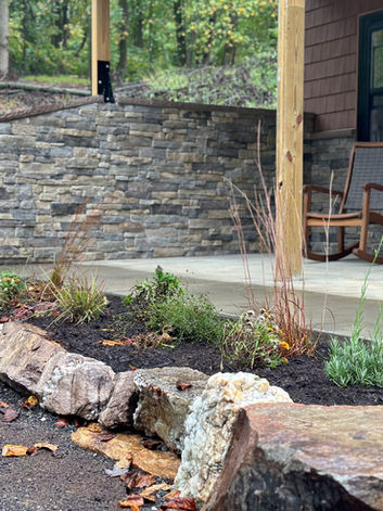 Stone wall, new landscaping, and porch with rocking chairs.