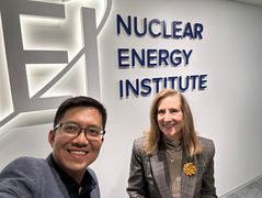 Tien Nguyen, Founding Partner of Earth Venture Capital and a Nuclear Energy Institute (NEI) representative smiling in front of the illuminated NEI logo and signage