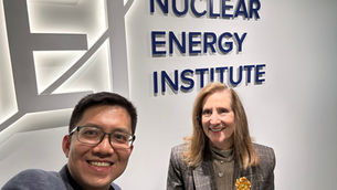 Tien Nguyen, Founding Partner of Earth Venture Capital and a Nuclear Energy Institute (NEI) representative smiling in front of the illuminated NEI logo and signage