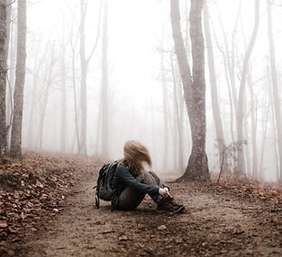 Image of a woman sitting in a fog-filled wooded area holding her knees