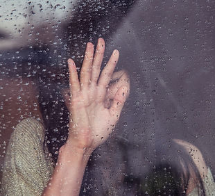 Image of a young woman with her eyes closed and palm pressed against a window