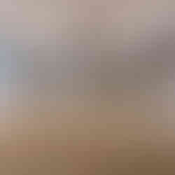 Covered wooden deck with a beadboard ceiling and ceiling fan, surrounded by railing and posts, overlooking a snowy wooded lakeside view with a neighboring house visible through the trees.