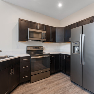 Finished kitchen with dark wood cabinetry, stainless steel appliances including a microwave, electric range, dishwasher, and side-by-side refrigerator with water dispenser. The countertops are light-colored. The flooring is wood-look vinyl planks.