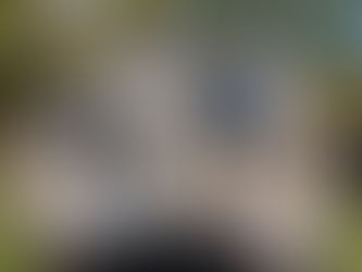 Exterior view of a house in East Stroudsburg, PA with light beige vinyl siding with white trim. The house has a sloped gray roof and a small porch with white columns. A garage is attached to the house, and the yard is freshly landscaped with grass and gravel. The surrounding area is wooded with trees.