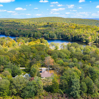 Exterior aerial view of a wooded neighborhood with a few homes nestled among trees, overlooking a blue lake and forested hills.