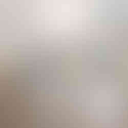 View of a kitchen and dining area with white cabinets, stainless steel appliances, and pendant lighting over the kitchen island. The flooring is a light wood laminate, and large windows provide natural light. A sliding glass door leads to a deck with a wooded view.