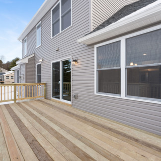 Exterior view of the back of a house in Reeders, PA with beige siding, windows, and a glass sliding door leading out to a large wooden back deck.