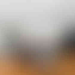 Interior view of a white kitchen with hardwood floors and a large waterfall-edge island topped with dark stone. Five bar stools line the island under two black pendant lights, with a skylight above and a matte-black refrigerator to the right near sliding doors to a screened porch.