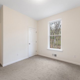 Unfurnished bedroom with gray carpet, cream-colored walls, and a single window overlooking a wooded area. The room has a standard ceiling light, two white paneled doors, closet and entry, and white baseboard trim.
