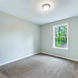 Unfurnished bedroom with light gray walls, gray carpet flooring, a flush-mount ceiling light, and a single window looking out to trees and a driveway.