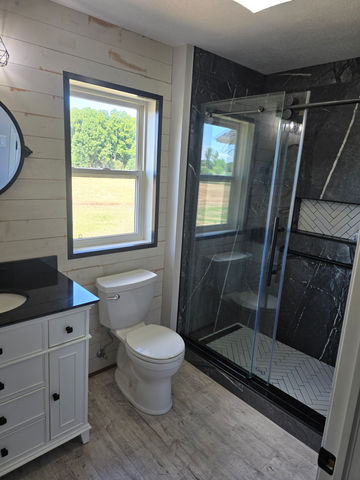 Modern bathroom remodel in Livingston County featuring white vanity with black countertop, wood-look flooring, and black tile