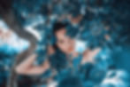 Woman peeks through vibrant blue leaves in a sunny garden, creating a serene and mysterious mood.