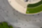 Vista aérea de uma praça curva e aberta, com pessoas espalhadas a caminhar por uma grande área circular pavimentada.